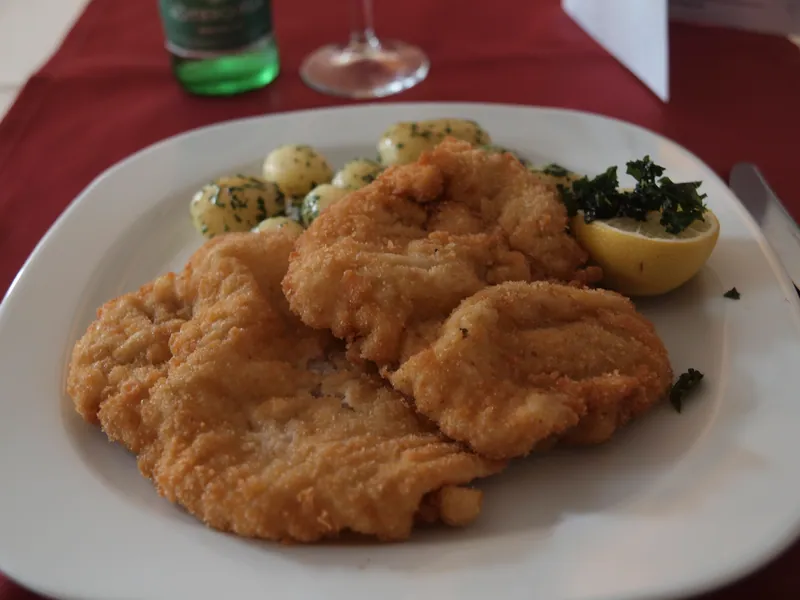Golden rippled veal Wiener schnitzel cutlets served with parsley potatoes and a lemon half on a white plate