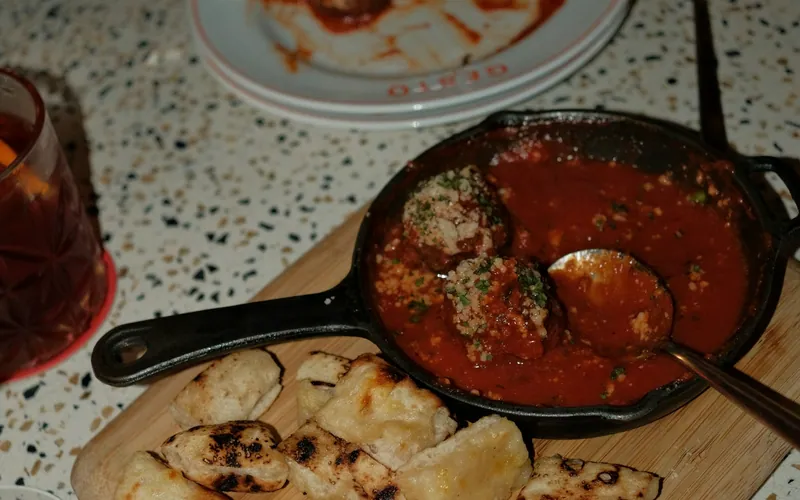 Chicken meatballs in tomato sauce with grated Parmesan and herbs in a cast-iron skillet beside pieces of toasted bread