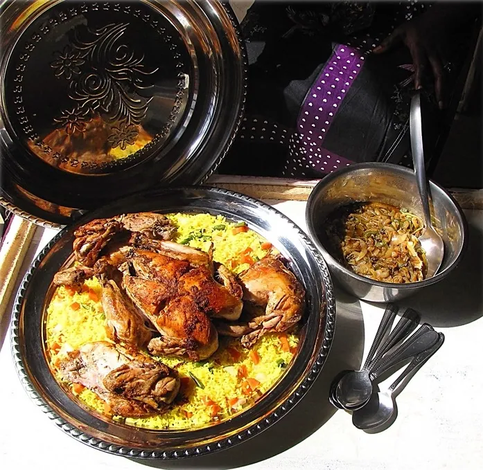 Browned chicken pieces on yellow rice with lemony onion sauce served in a bowl alongside