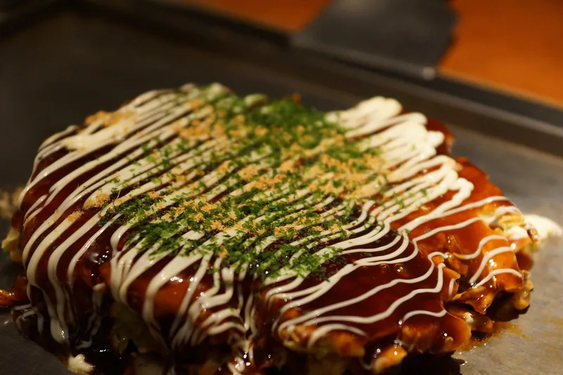 Two Osaka-style okonomiyaki pancakes covered with dark sauce, white mayonnaise stripes, green aonori and bonito flakes