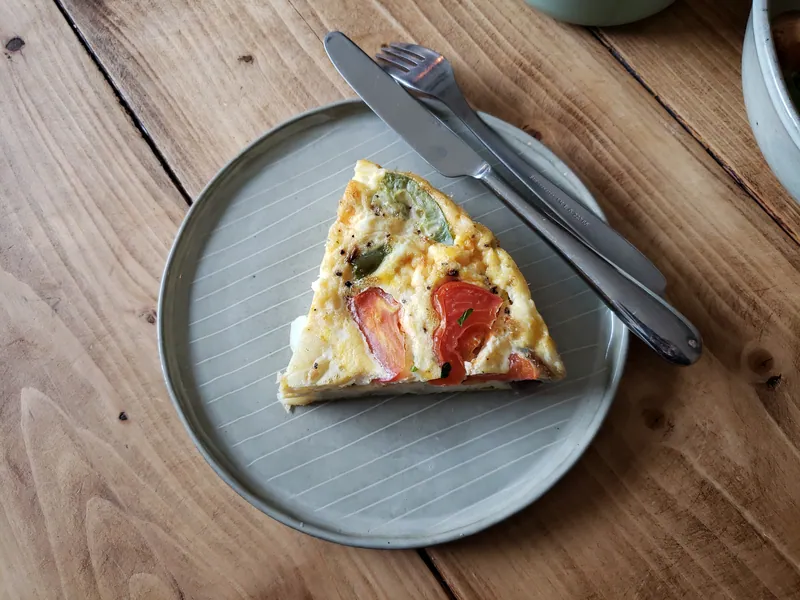 Slice of golden frittata with roasted tomato wedges and green pepper pieces on a gray plate