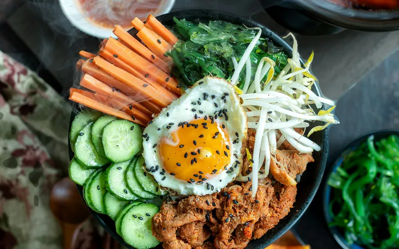 Beef bibimbap bowl with rice, a fried egg, carrots, cucumber, bean sprouts, seaweed and black sesame seeds