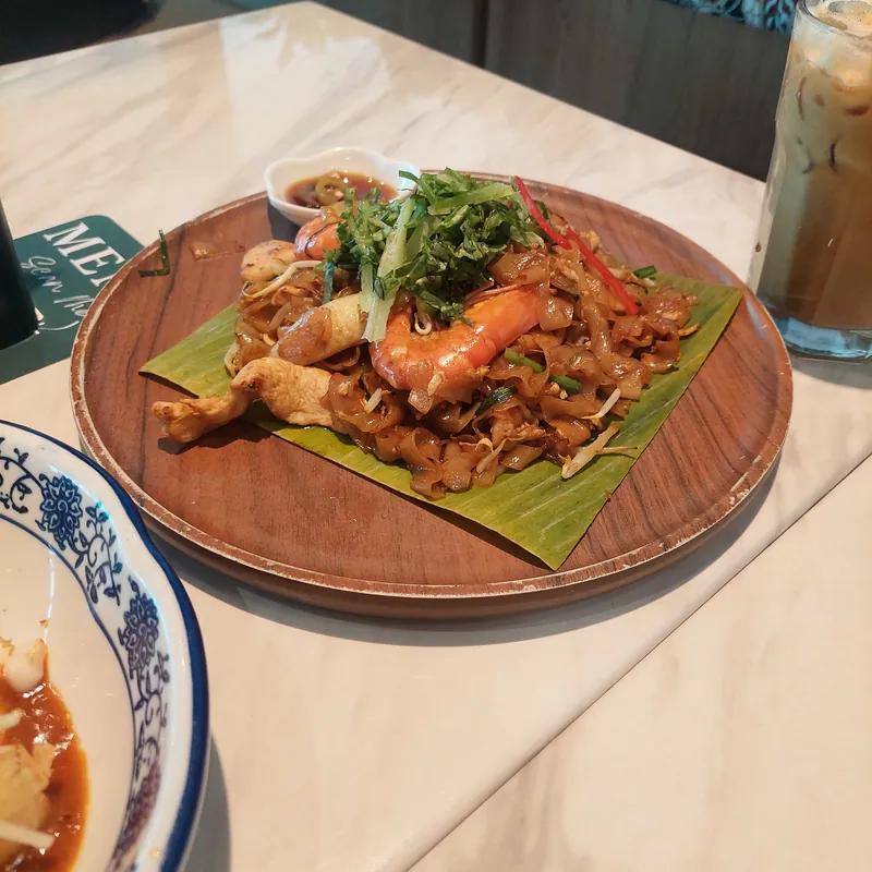 Malaysian-style char kway teow with wide rice noodles, whole prawns, chicken, bean sprouts and chives on a banana-leaf-lined plate