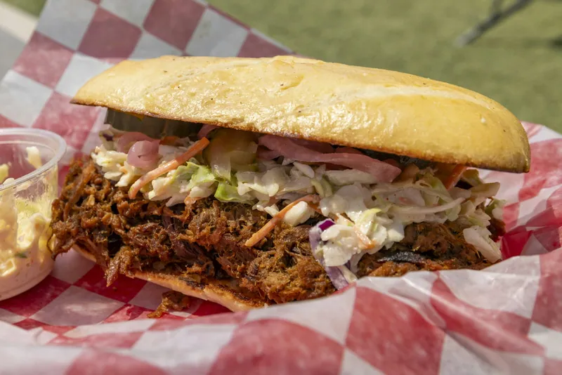 Pulled pork sandwich topped with creamy cabbage slaw, dill pickles and pickled red onion