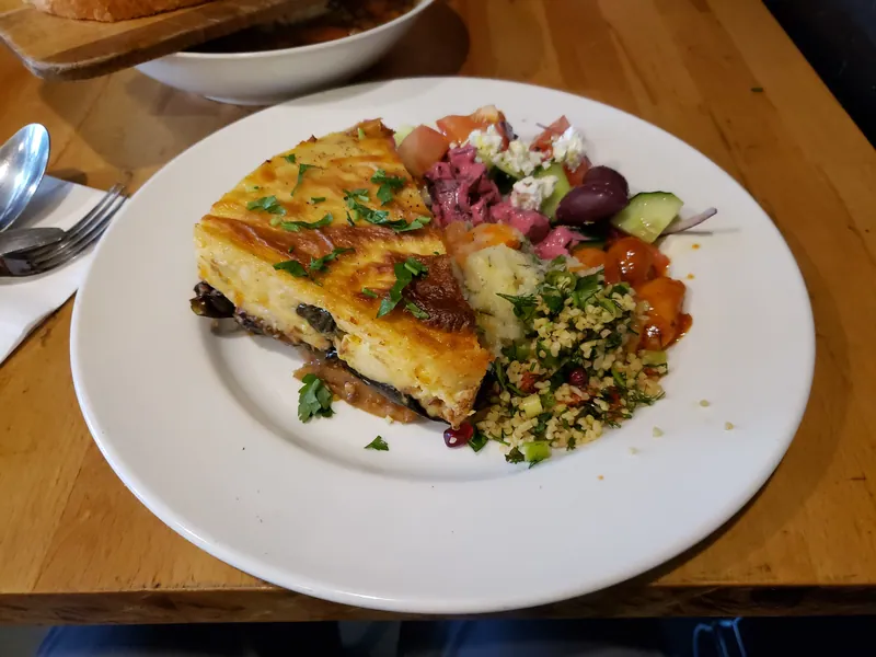 Thick square of lamb and eggplant moussaka with a golden béchamel top served beside a green salad