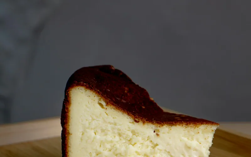 Thick slice of crustless burnt Basque cheesecake with a deeply caramelized dark top and creamy pale center on a wooden board