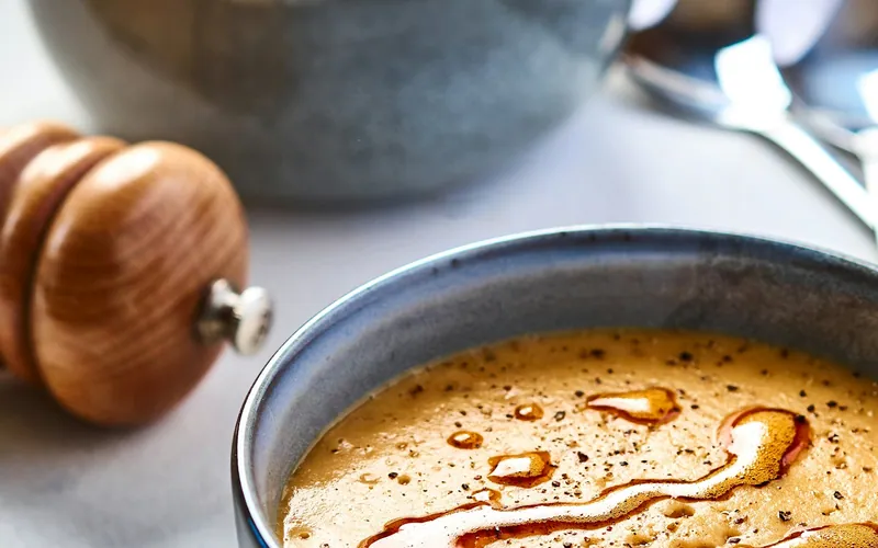 Creamy orange-red lentil soup in a dark bowl with a glossy red Aleppo-butter swirl and black pepper