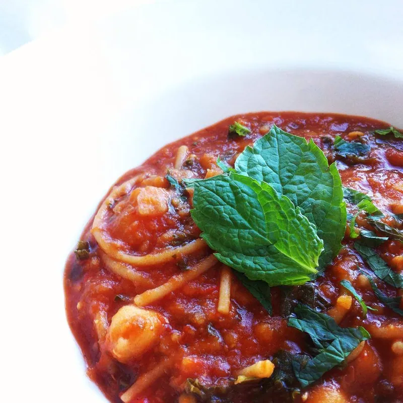 Thick red tomato harira with chickpeas, fine vermicelli and fresh mint in a white bowl