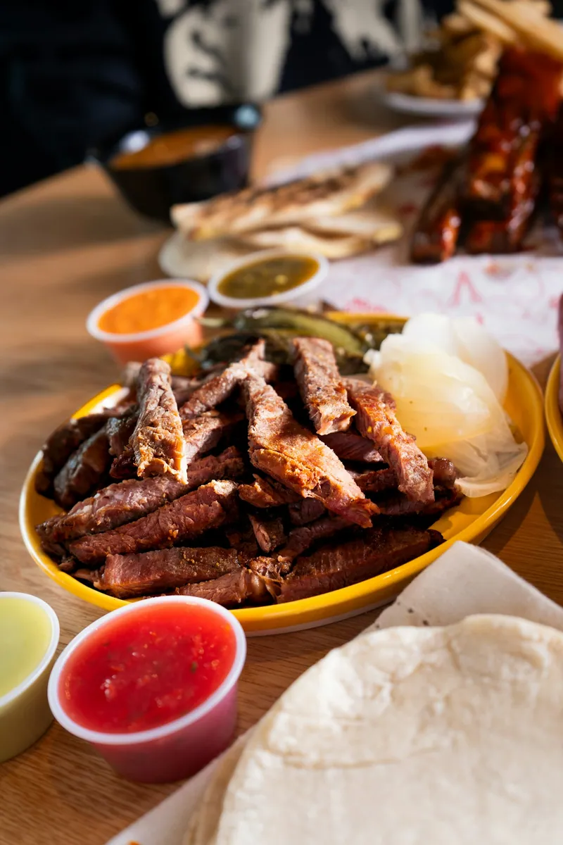 Sliced grilled beef fajitas with charred onions, salsa, lime, and warm tortillas