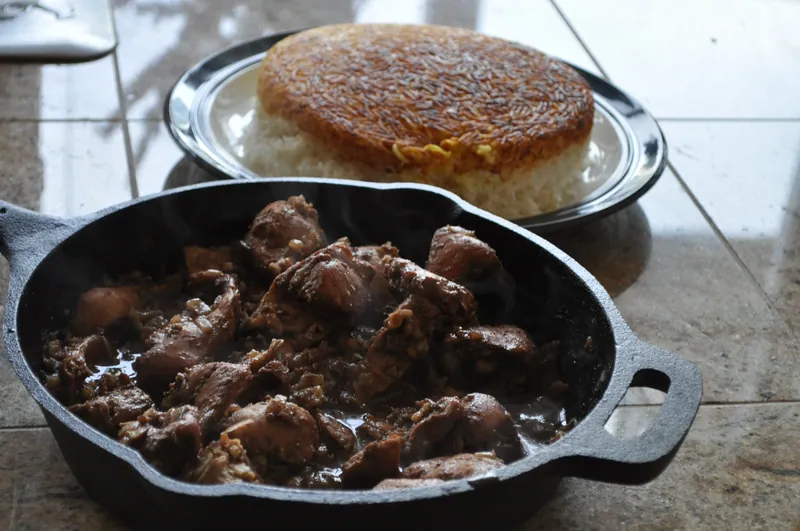 Dark walnut-pomegranate chicken fesenjan stew in a skillet beside a bowl of white rice
