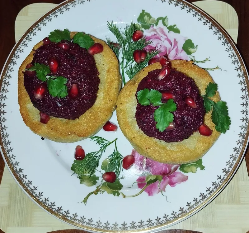 Deep-red beet pkhali mounds on two golden mchadi corn cakes with pomegranate seeds, cilantro and dill