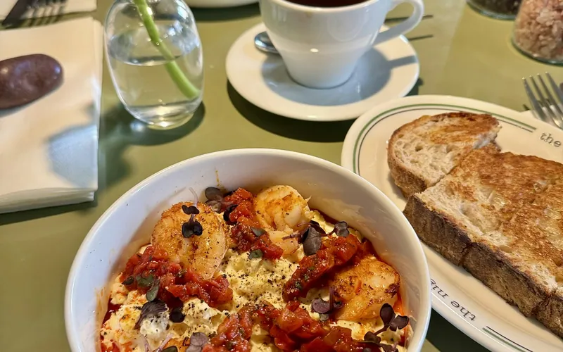 Seared shrimp over creamy cheddar grits with a chunky red tomato sauce, black pepper, and tender microgreens in a white bowl