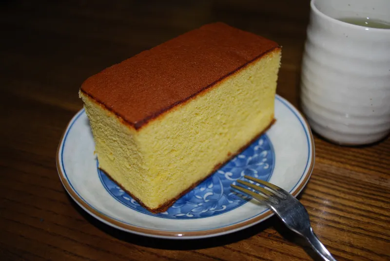 Tall rectangular slice of Nagasaki-style castella with a dark brown top and fine golden honey sponge crumb