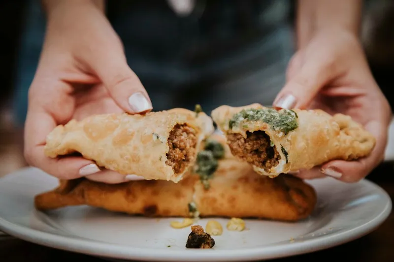 Two crisp fried beef empanadas pulled open to show the ground beef filling, topped with green parsley chimichurri
