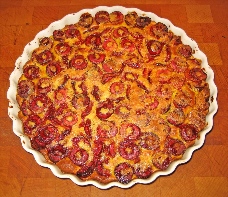 Round golden French cherry clafoutis filled with visible halved red cherries in a white fluted baking dish