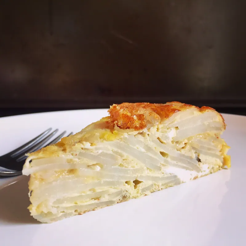 Cut wedge of Spanish tortilla showing distinct layers of tender potato bound with golden egg