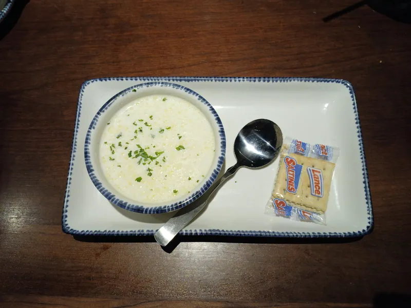 Creamy New England clam chowder sprinkled with parsley in a small bowl beside packaged saltine crackers