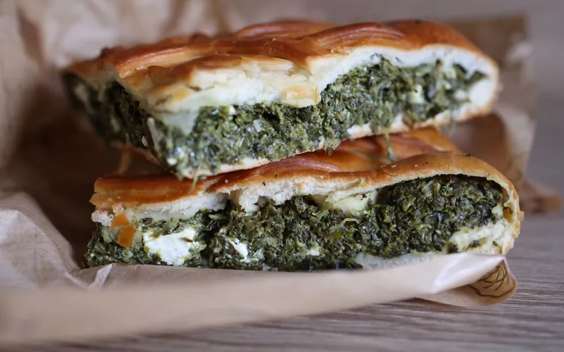 Thick slices of golden lattice pie filled with dark green spinach, white feta and herbs on parchment