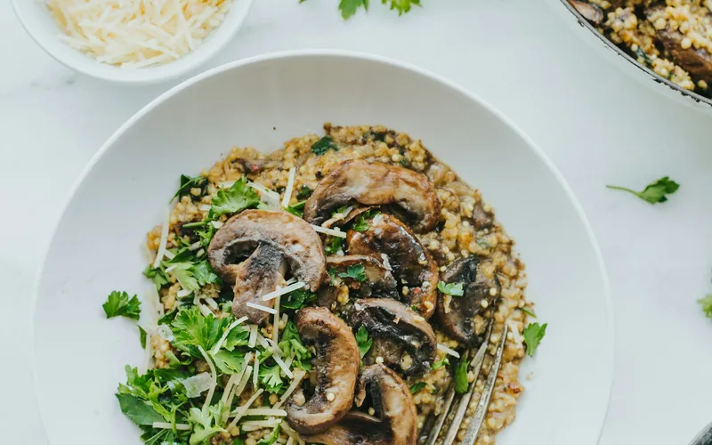 Creamy mushroom risotto topped with browned sliced mushrooms, finely shredded Parmesan, chopped parsley, and black pepper on a white plate