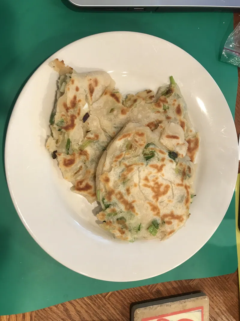 Four rustic round scallion pancakes with browned blistered surfaces and visible green onion pieces on a white plate