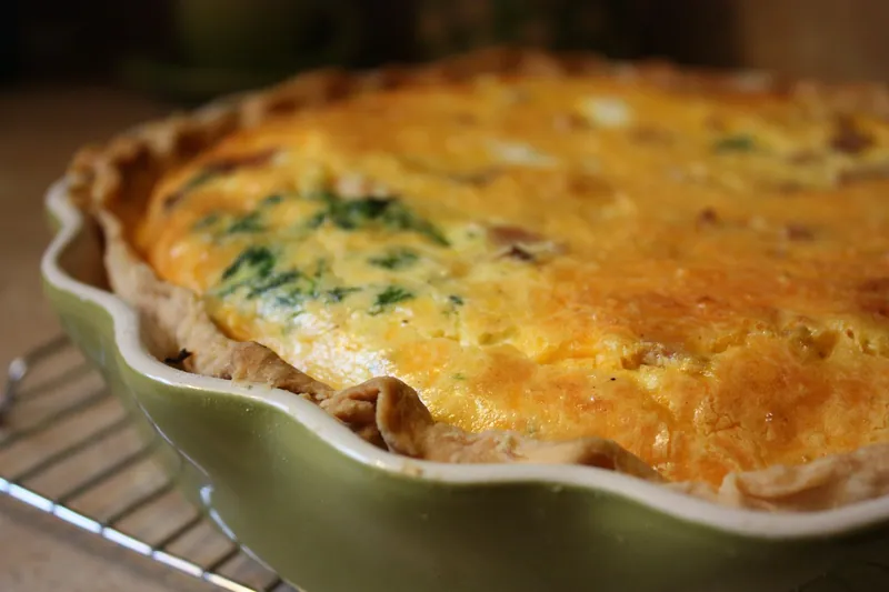 Golden baked spinach, onion, and cheddar quiche in a fluted pie dish with a browned flaky pastry crust