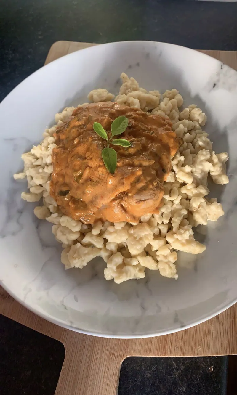 Hungarian chicken paprikash with orange-red sour-cream paprika sauce over small hand-cut egg dumplings, garnished with fresh herbs